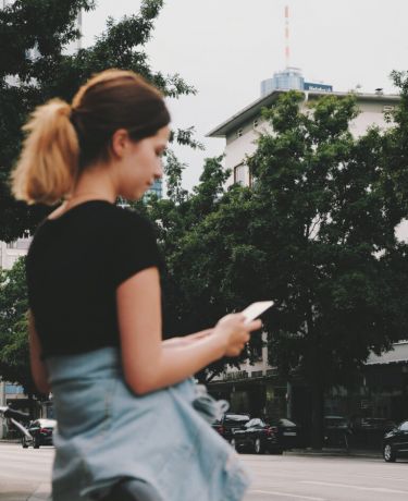 Teammitglied Franzi wartet mit Smartphone an der Straße auf ihr Taxi