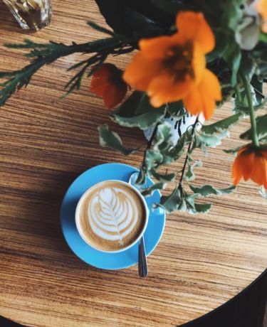 Eine blaue Tasse mit Latte Art und ein Blumenstrauß