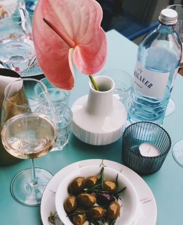 Oliven, Wasserflasche und Weißweinglas auf einem blauen Tisch