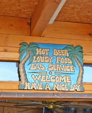 Schild mit Aufschrift "Hot Beer, Lousy Food, Bad Service: Welcome, have a nice day"